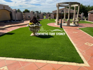 Man installing synthetic turf in a backyard garden with a gazebo.
