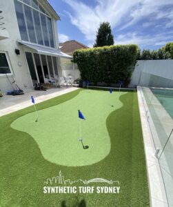 A backyard putting green with flags and a glass fence under a sunny sky.