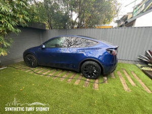 Blue Tesla Model 3 parked on grass with black wheels.