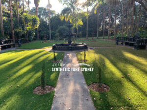 Sunlit garden path leading to a central fountain surrounded by green lawns.