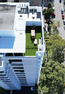 Rooftop terrace with green lawn and lounge seating overlooking city streets.