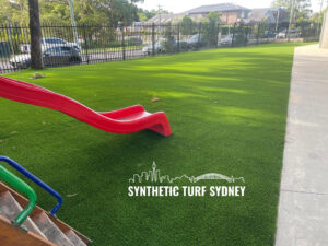 Bright green synthetic turf with a red slide in a sunny playground.