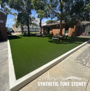 Well-maintained synthetic turf lawn in a sunny backyard with trees and buildings.