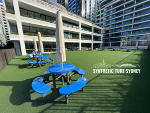 Blue picnic tables on synthetic turf in a modern urban courtyard.