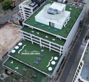 A rooftop garden with lounge chairs and greenery on a multi-story building.