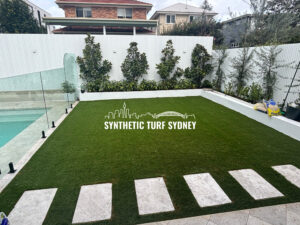 A neatly maintained synthetic turf lawn with stepping stones and a glass fence.