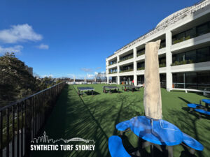 Outdoor seating area with blue umbrellas and synthetic turf under a clear sky.